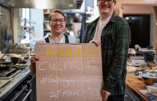 A woman and a man holding a cardboard sign saying Culprit #cookingupastorm 20th March '23